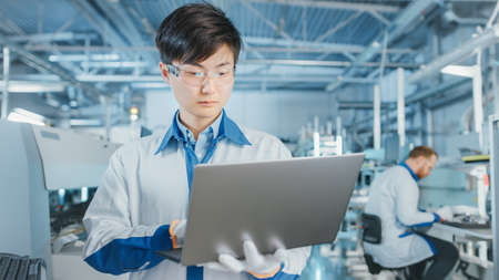 On High-Tech Factory Asian Engineer Uses Laptop Computer for Programing Pick and Place Electronic...