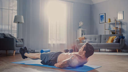 Strong Athletic Shirtless Fit Man in Grey Shorts is Doing Abdominal Exercises at Home in His...