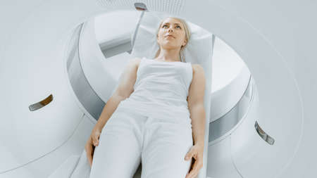 Close-up Portrait of a Female Patient Lying on a CT or MRI Scan, Bed is Moving inside Machine Scanning Her Body and Brain. In Medical Laboratory with High-Tech Equipment.の写真素材