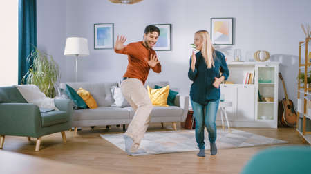 Beautiful Happy Young Couple in Love Dancing in the Middle of the Living Room. Boyfriend and Girlfriend Cheerfully Celebrate by Dancing at Home.の写真素材
