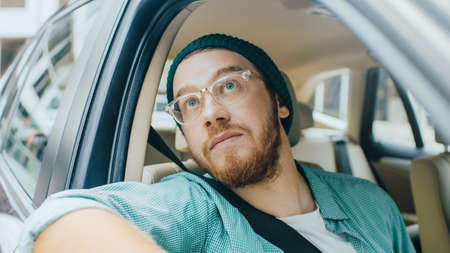 Stylish Young Man Rides on a Passenger Seat of a Car and Looks in Open Window in Wonder Up at the...