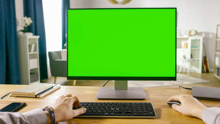 First Person View of Professional Freelancer Working on Green Mockup Screen Personal Computer From Home. Close-up POV Shot. In the Background Cozy Living Room.の写真素材