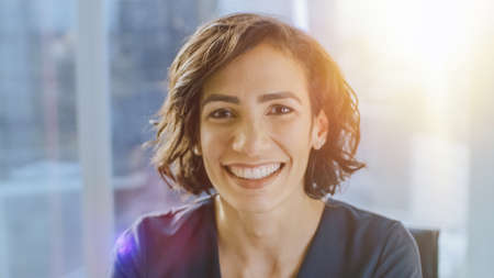 Portrait of a Beautiful Hispanic Woman Smiling Charmingly at Camera. Out of Focus Background with Sun Flares.の写真素材