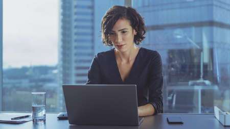 Beautiful Successful Female CEO Works on a Laptop in Her Modern Sunny Office with Cityscape Window...