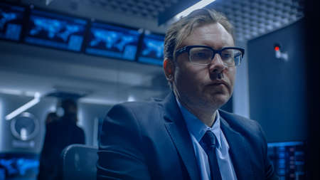 Low Angle of the Concerned Specialist Working on Computer in the Monitoring Control Room with Teams...