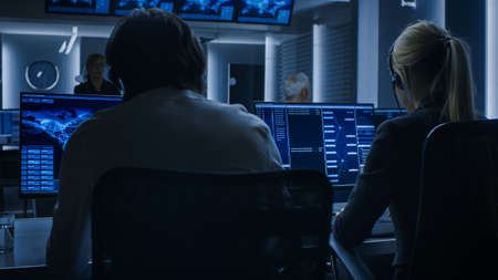 Back View of the Cyber Security Dispatchers Working on Personal Computer Showing Traffic Data Flow in the System Control Room full of Special Intelligence Agents.の写真素材
