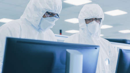 Two Scientists Technicians in Sterile Suits Check Data on Personal Computer, the Have Discussion....
