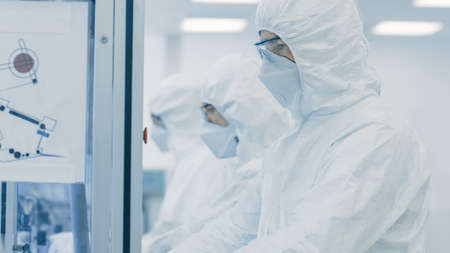 On a Factory Team of Scientists in Sterile Protective Clothing Work on a Modern Industrial 3D Printing Machinery. Pharmaceutical, Biotechnological and Semiconductor Creating Manufacturing Process.の写真素材