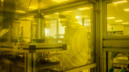 In Manufacturing Facility Shot of Scientist in Sterile Protective Clothing Work on Industrial 3D Printing Machinery. Biotechnological Manufacturing Process. Shot from Inside with Yellow Light Filter.の写真素材