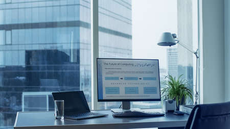Shot of the Office Desk with Personal Computer Standing on It. Future Computing Plans Shown on Monitor. Modern Stylish Room with a Big City Business District View.の写真素材