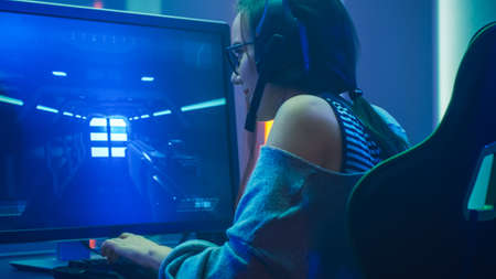 Shot of the Beautiful Pro Gamer Girl Playing in FPS Video Game on Her Personal Computer, Casual Cute Geek wearing Glasses and Headset. Neon Room. Online Cyber Games Internet Championship Event.の素材 [FY310158113696]