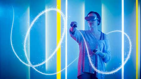 Beautiful Young Girl Wearing Virtual Reality Headset Draws Abstract Lines and Figures with Joysticks...