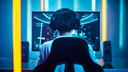 Back Shot of the Professional Gamer Playing in First-Person Shooter Online Video Game on His...
