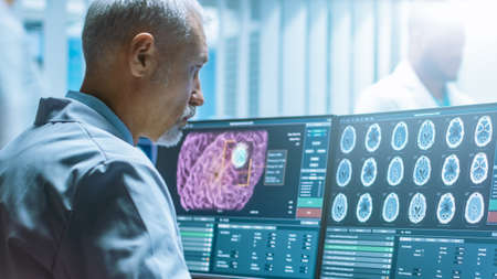 Senior Medical Research Scientist Working with Brain Scans on His Personal Computer. Modern Laboratory Working on Neurophysiology, Science, Neuropharmacology. Understanding Human Brain.の写真素材