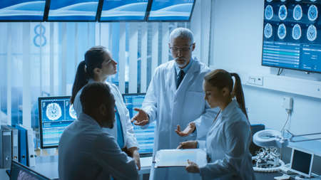 Meeting of the Team of Medical Scientists in the Brain Research Laboratory. Neurologists Neuroscientists Having Analytical Discussion Surrounded by Monitors Showing CT, MRI Scans.の写真素材