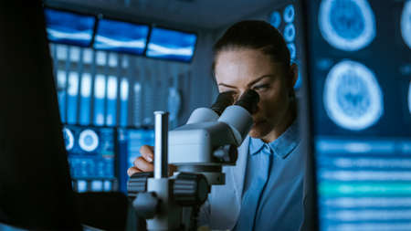 Female Medical Research Scientist Looking Through the Microscope Types Acquired Data in the...