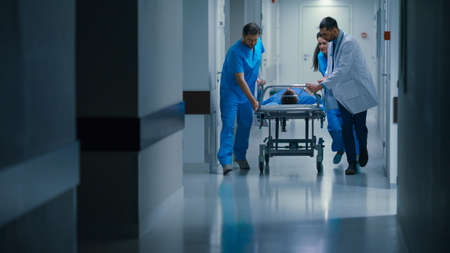 Emergency Department: Doctors, Nurses and Paramedics Push Gurney Stretcher with Seriously Injured Patient towards the Operating Room. Bright Modern Hospital with Professional Staff Saving Lives.の写真素材