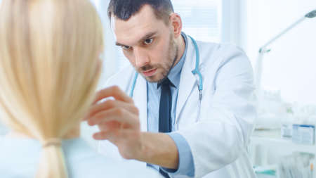 Over the Shoulder Shot of a Female Patient Sitting Patiently While Plastic Cosmetic Surgeon Draws Lines on Her Face for Facelift Operation.の写真素材
