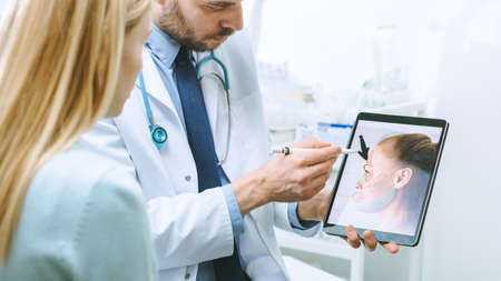 Plastic Cosmetic Surgeon Consults Woman about Facial Lift Surgery, He Points at Digital Tablet...