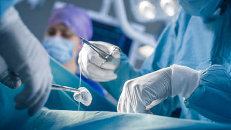 Close-up on Hands of the  Professional Surgeon Suture Wound after Successful Surgery. In the Background Modern Hospital Operation Room.の写真素材