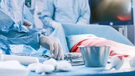 Close-up Shot in the Operating Room of Surgical Table with Instruments, Assistant Hands out Instruments to Surgeons During Operation. Surgery in Progress. Professional Medical Doctors Performingの写真素材