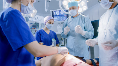In the Hospital Operating Room Anesthesiologist Applies Anesthesia Mask to a Patient, Assistants Disinfects with Iodine place of Incision, Surgeons Wait to Start Surgery.の写真素材