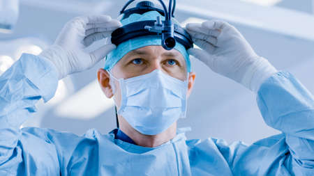 In the Hospital Operating Room Professional Surgeon Puts on Surgical Flashlight, Before Surgery...