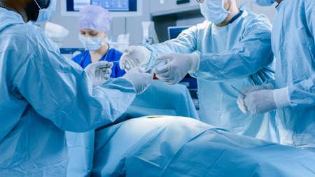 Diverse Team of Professional Surgeons Performing Invasive Surgery on a Patient in the Hospital...