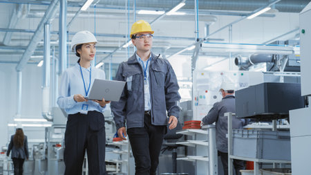Two Young Asian Heavy Industry Engineers in Hard Hats Walking with Laptop Computer and Discussing...
