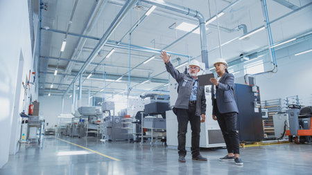 Portrait of Two Heavy Industry Employees in Hard Hats at Factory. Checking and Discussing Industrial...