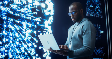 Portrait of Young Black Man Working on Laptop Computer, Looking at Big Digital Screen Displaying Neural Network Visualisation in 3D. Professional Data Specialistの素材