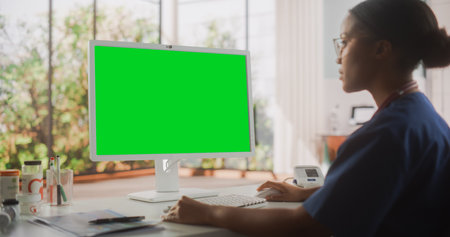 Portrait of a Black Female Medical Health Care Professional Working on Desktop Computer with Green Screen Mock Up Display in Hospital Office. Clinic Head Nurse isの写真素材