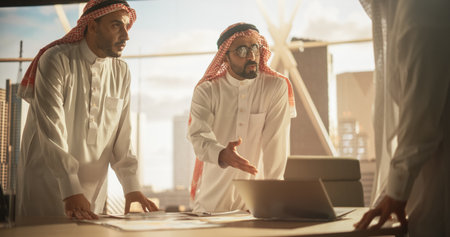 Successful Muslim Businessmen in White Traditional Outfits Having an Office Meeting, Negotiating and Talking About Financial Opportunities. Using Laptop. Saudi, Emirati,の写真素材