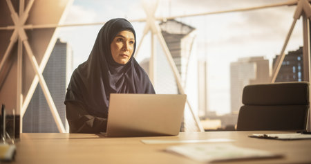 Portrait of a Young Female Business Account Manager Working on a Laptop Computer in a Modern Corporate Office. Businesswoman Dealing with Financial Reports, Preparing a Growth Planの写真素材