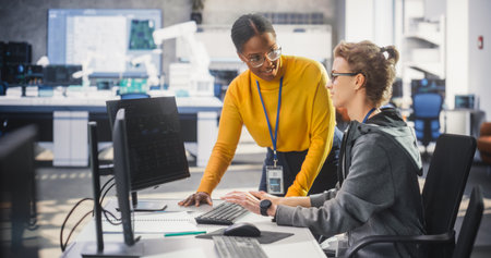 African Female Manager Having a Conversation with Young Intern Specialist in a Creative Agency, Collaborating on a Technology Project. Diverse Young Professionals Preparingの写真素材