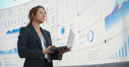 Successful Hispanic Businesswoman Holding Laptop Computer And Reviewing Financial Reports On Digital Screen In Monitoring Office. Female Leader Running Deep Learning, Artificialの写真素材