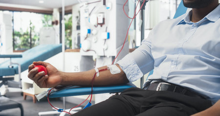 Close Up Shot Of Hand Of Black Male Blood Donor With an Attached Catheter. African Businessman Squeezing Heart-Shaped Ball To Pump Blood Through Tubing Into Bag. Donation Forの写真素材