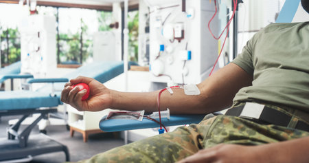 Close Up Of Hand Of Black Army Soldier With Attached Catheter In Military Hospital. Brave African Male Troop Sqeezing Red Ball To Pump Blood Through Tubing Into Bag. Man Donatingの写真素材