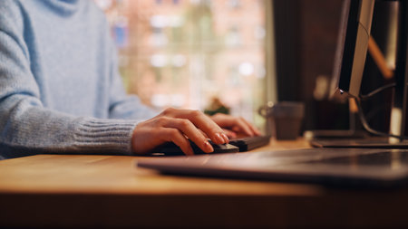Close Up Footage of Person's Feminine Hands Use Computer while Sitting at a Table. Creative Designer in Blue Sweater Using Mouse, Typing on Keyboard. Monitor Display and Laptopの写真素材