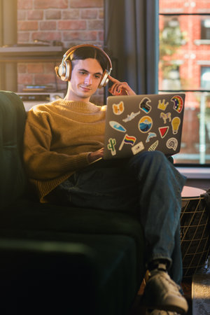 Vertical Screen: Young Handsome Man Working from Home on Laptop Computer in Stylish Loft Apartment...
