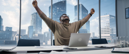 Black Businessman Sitting at His Desk in Skyscraper Office and Works on Laptop, Emotionally Celebrates Success in e-Business Deal. African American Entrepreneurの写真素材