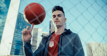 Portrait of a Handsome Young Football Player Looking at Camera, Spinning a Red Soccer Ball on His...