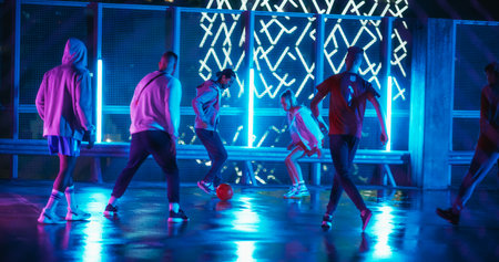 Friends Playing Soccer at a Stylish Spot with Neon Lights and Skyscrapers at Night. Young Football Player Dribbling, Showing Off Tricksの写真素材