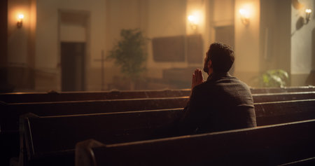 Christian Man Sits Alone in Church, Praying, Seeks Guidance from Religious Faith and Spiritual Belief in the Lord. Cinematic Camera Capturing the Spirit of Christianity andの写真素材