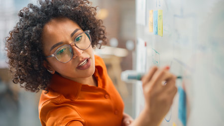 Modern Creative Agency Meeting: Confident Black Female Engineer Uses Whiteboard, Makes Report to a...