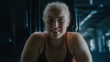 A Fit Young Woman Smiling Happily After Finishing Working Out and Training in a Dark Gym. A...