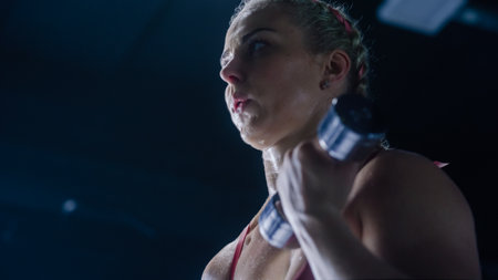 A Female Kickboxer Building her Arms' Muscles Using Dumbbell Exercises in an Empty Hardcore Gym. A Resilient Female Sports Champion Training and Working Out inの写真素材