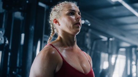 Close up on the Face of a Beautiful Female Athlete in a Dark Gym . Strong Female Bodybuilder Focused on her Exercises and Workout while Trainingの写真素材