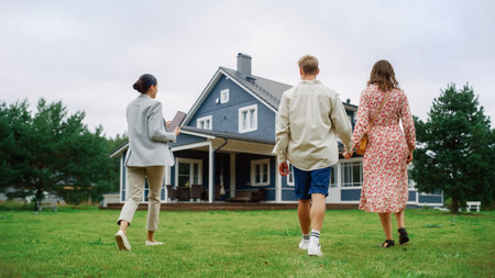 Young Couple Viewing Property for Sale, Talking with Professional Real Estate Agent Outside the House on a Summer Day. Young Beautiful Family are Ready toの写真素材