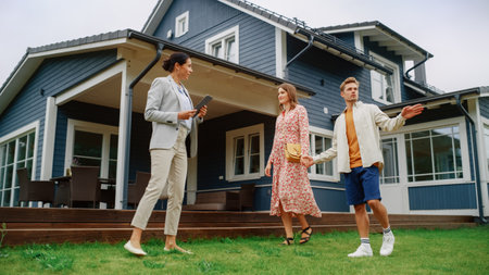 Young Couple Visiting a Potential New Home Property with Professional Real Estate Agent. Realtor Showing a Beautiful Modern House with Traditional Suburban Design to a Youngの写真素材
